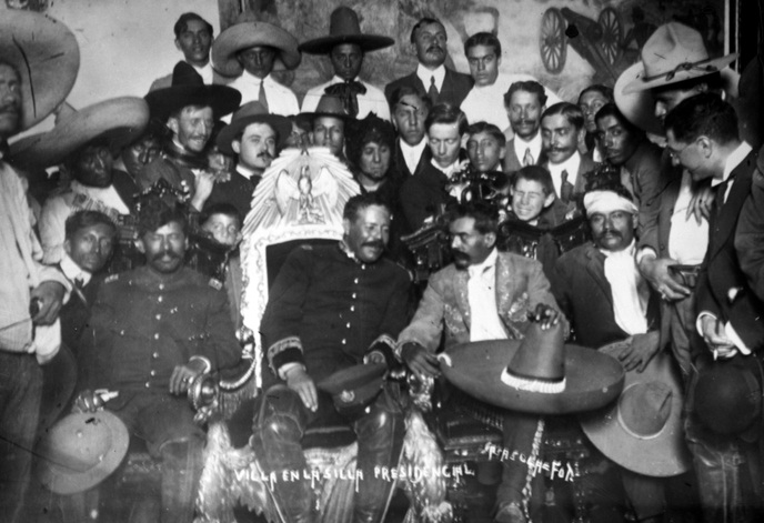 Pancho Villa seated in the presidential chair beside Emiliano Zapata, surrounded by soldiers